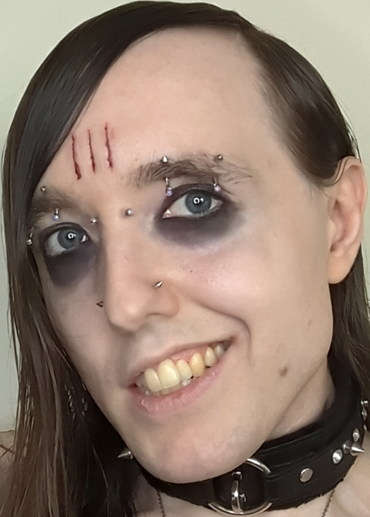 A close-up photo of Violet Alice Rose against a light background. It has pale skin and long, oily dark brown hair parted sharply to the right, with no bangs. It has medium blue eyes with dark eyeshadow extending down to the under-eye area, creating a sunken look. Its face features multiple piercings: a bridge piercing with round jewelry caps, two equidistant eyebrow piercings on each eyebrow with round jewelry caps on the bottom and small spikes on top, and nostril piercings with spiked caps. A mark consisting of three vertical scars is visible on the lower forehead, crusted with dried blood. It has a mole on the left side of its jaw, slightly chapped lips, and a confident, asymmetrical grin with a slight overbite, its mouth open wider to the left than the right. It's wearing a heavy black leather spiked choker.